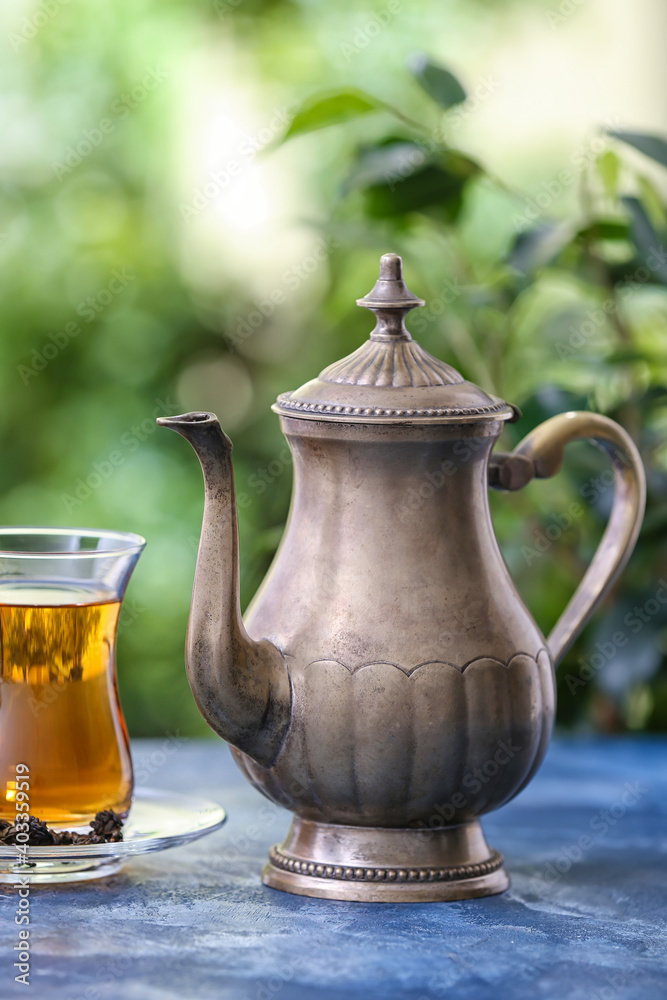 Teapot and glass with tea on table against blurred background Teapot and glass with tea on table against blurred background