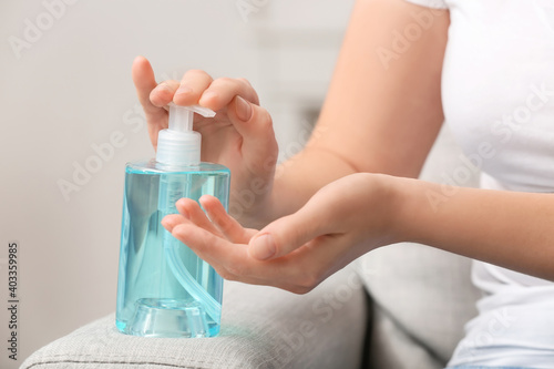 Young woman using sanitizer at home, closeup
