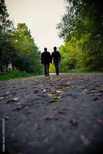  male gay couple  holding hands walking in the park on a cloudy afternoon with autumn eyes on the floor