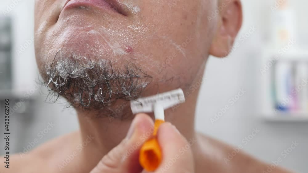 Reusing Face Razor Men Handsome young man with foam on his face shave using razor in bathroom ...