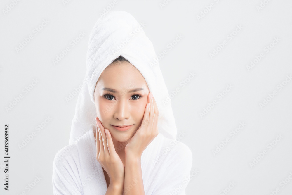 Beautiful young woman wearing bathrobe with towel on head with healthy skin is touching her skin with satisfaction is at studio shot isolated on white background. Beautiful young woman wearing bathrobe with towel on head with healthy skin is touching her skin with satisfaction is at studio shot isolated on white background.