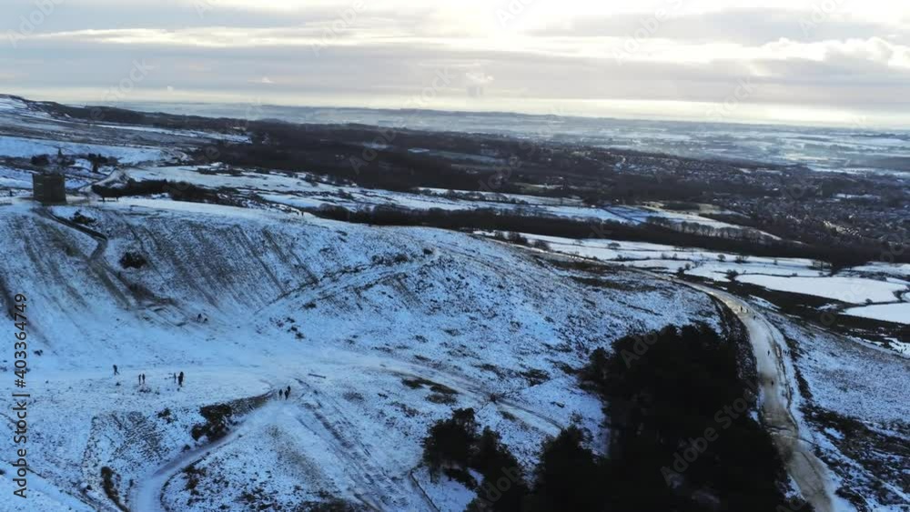 Snowy Rivington Pike tower Winter hill aerial slow pan right view people sledding downhill at sunrise Snowy Rivington Pike tower Winter hill aerial slow pan right view people sledding downhill at sunrise