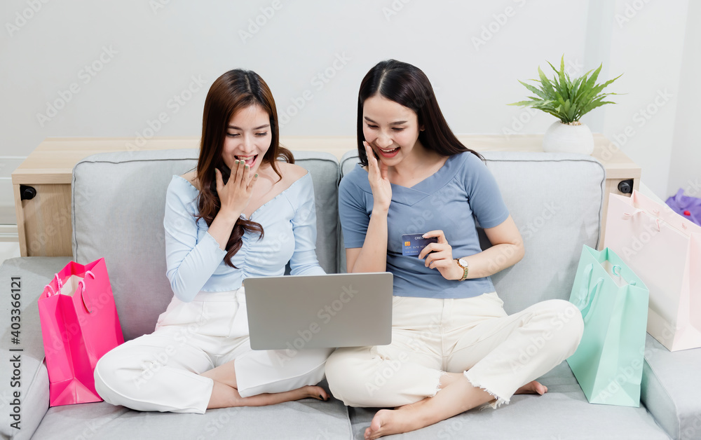 Two Asian beauty people are using a credit card to make purchases using a laptop via the internet. With a happy smiling face, being a new normal online business In the shopping experience from home Two Asian beauty people are using a credit card to make purchases using a laptop via the internet. With a happy smiling face, being a new normal online business In the shopping experience from home