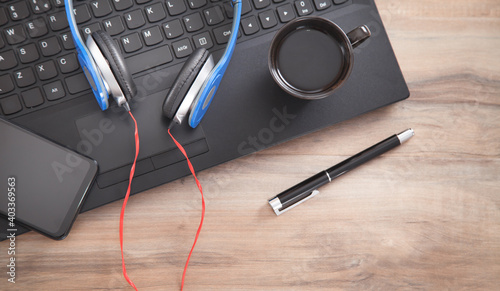 Headphones, pen, smartphone coffee with a laptop keyboard.