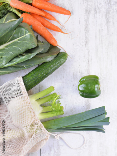 vegetables in a reusable  bag  among other  fresh vegetables  on a white table