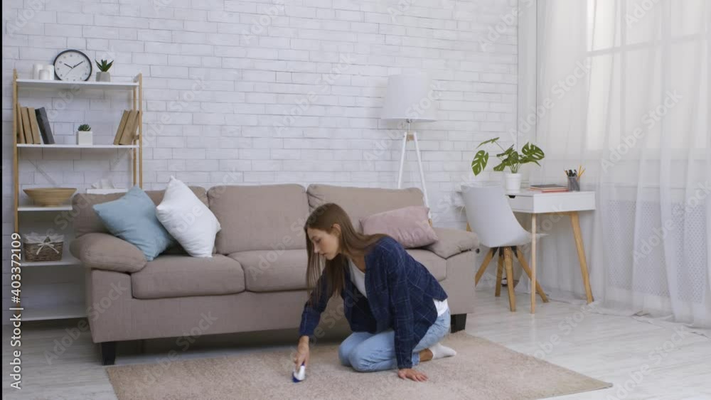 Housekeeping concept. Young woman brushing carpet at home, sitting on floor Housekeeping concept. Young woman brushing carpet at home, sitting on floor