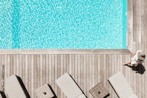 Woman with hat walk on the wooden terrace near the swimming pool