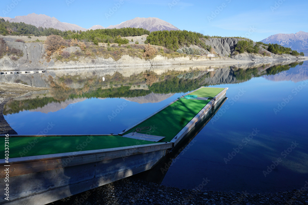 mirror reflection of the mountains in Serre Ponçon lake, France from a small metallic pier with fake green lawn