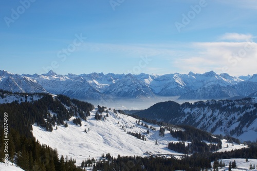 Winterlandschaft der schneebedeckten bayerischen Alpen über Wolken vor blauem Himmel