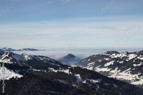 Winterlandschaft der schneebedeckten  bayerischen Alpen über Wolken vor blauem Himmel