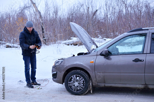 car repair on the road in winter. a young man is trying to fix a car breakdown under the soot on the road. woodsroadside assistance car