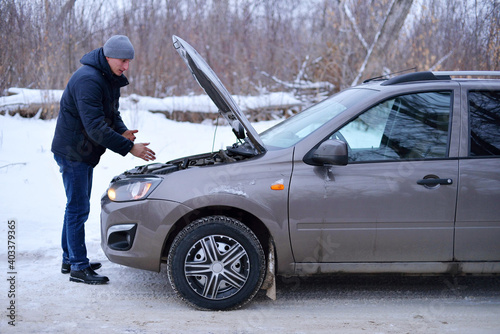 car repair on the road in winter. a young man is trying to fix a car breakdown under the soot on the road. woodsroadside assistance car.