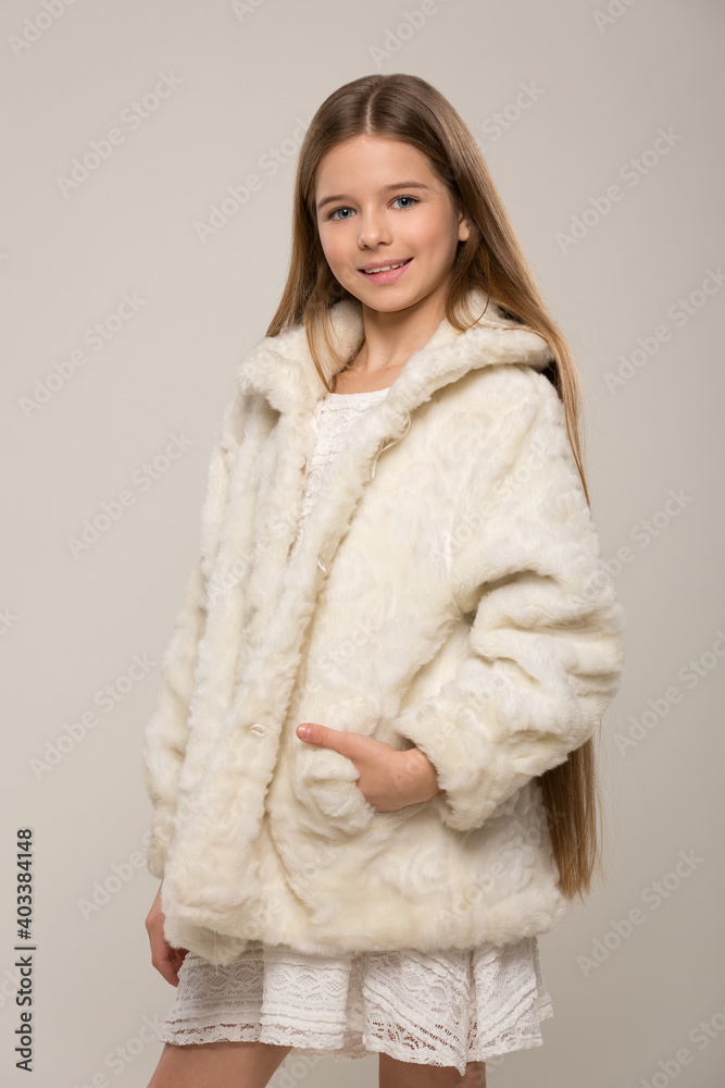 beautiful child girl with long hair in a white dress and short fur coat posing on a white background beautiful child girl with long hair in a white dress and short fur coat posing on a white background