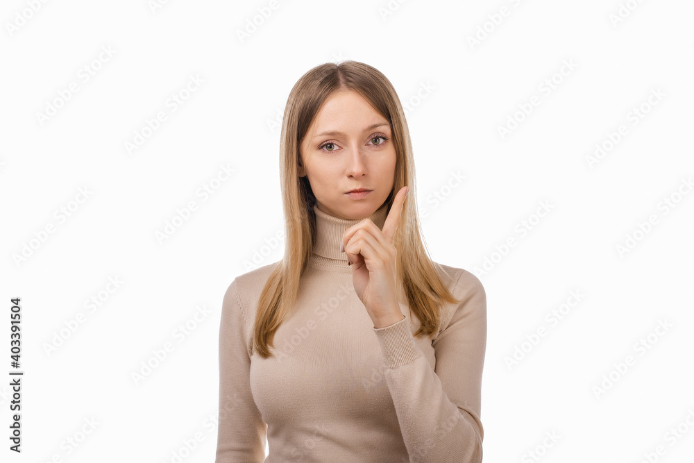 Portrait of Serious young blond woman showing index finger. Girl raises finger up, says: Attention please Portrait of Serious young blond woman showing index finger. Girl raises finger up, says: Attention please