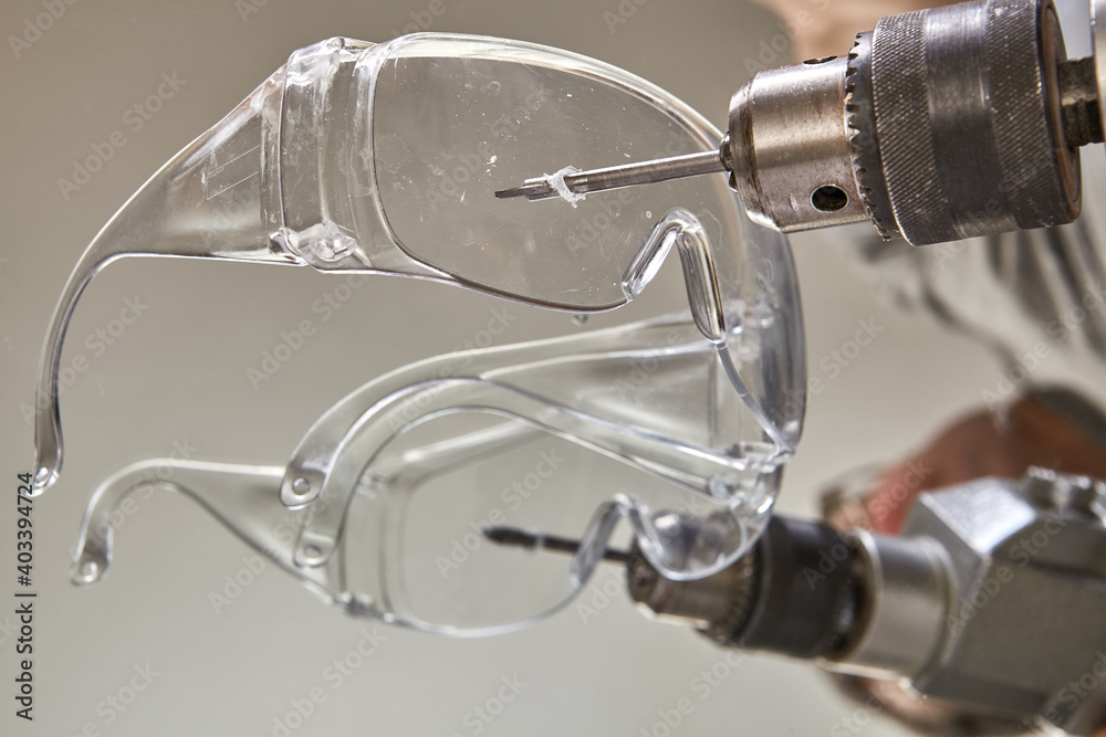 Safety glasses are pierced with drill for drilling holes in glass while drilled mirror. Safety glasses are pierced with drill for drilling holes in glass while drilled mirror.