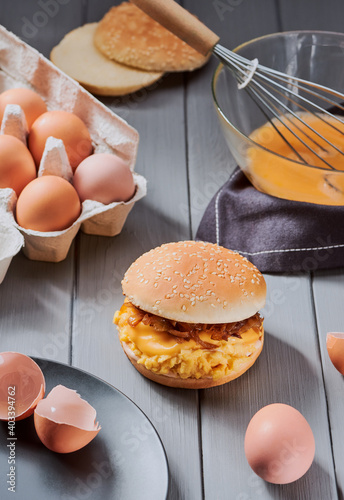 Eggs, bowl, whisk and finished burger on gray background photo