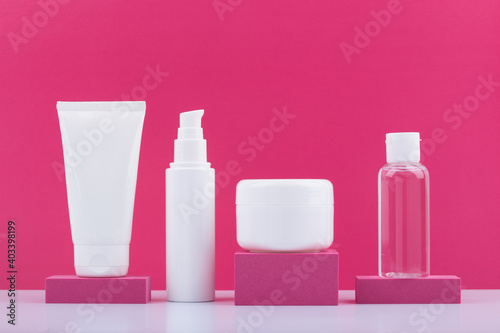 Set of cosmetic products in unbranded glossy white jars on pink podiums against bright pink background. Concept of beauty routine and skincare or anti aging treatment