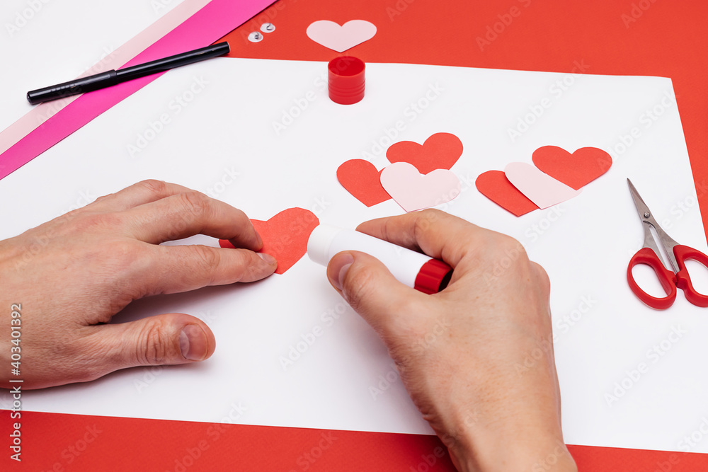 Men's hands make a paper caterpillar of colored paper hearts. Step-by-step instructions, step 7. Gift concept for Valentine's day and Mother's day. Men's hands make a paper caterpillar of colored paper hearts. Step-by-step instructions, step 7. Gift concept for Valentine's day and Mother's day.