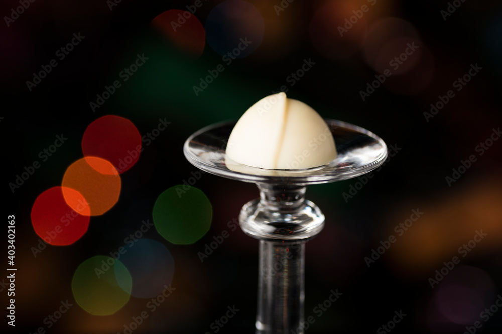 Selective focus shot of white chocolate candy on a glass stand on bokeh background
