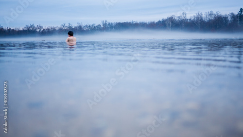 Man taking an ice bath in a lake.  Forrest in the winter haze. Cold water and low temperature.