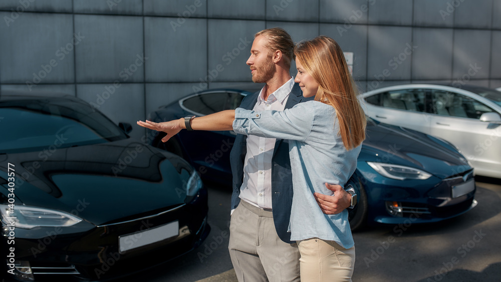 Happy young woman pointing at car in showroom Happy young woman pointing at car in showroom