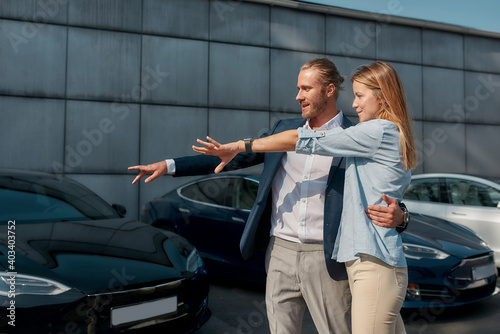Young couple pointing at car while hugging in showroom © Svitlana