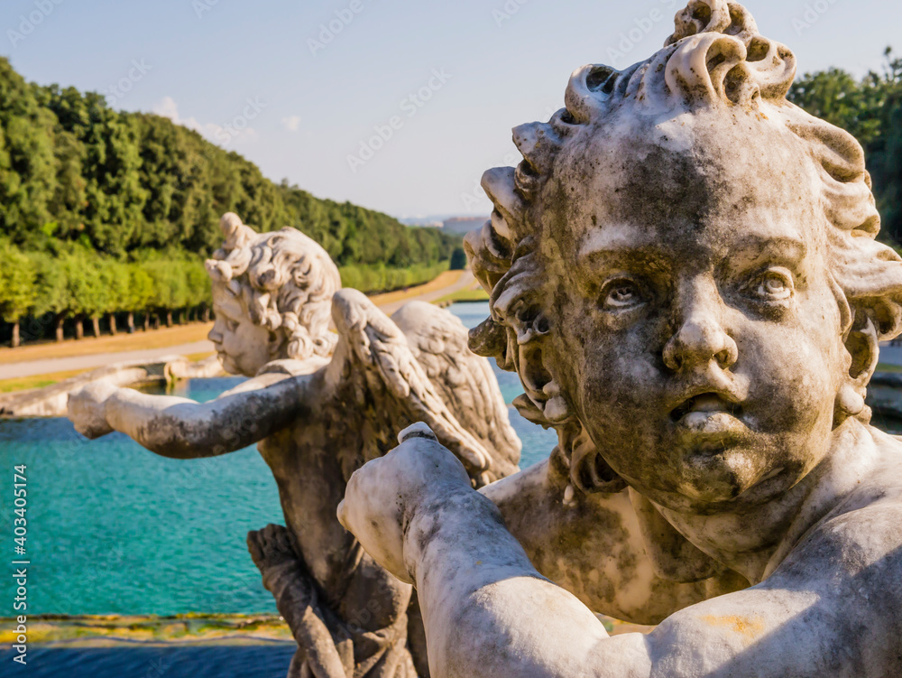 Detail of the fountain of Venus and Adonis with the face of a winged marble cherub in the foreground, Royal Palace of Caserta, Italy
