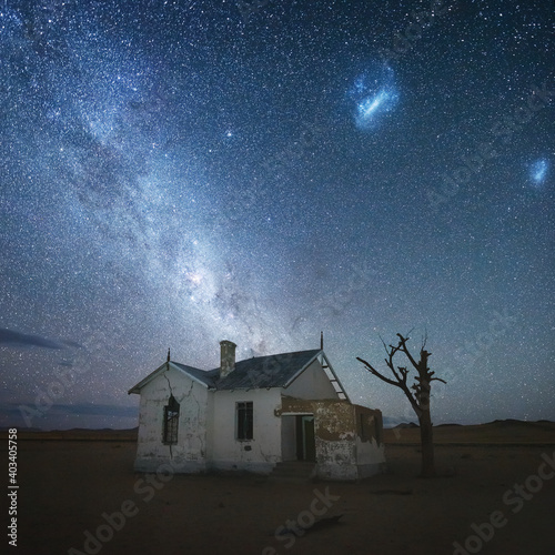 Fototapeta Naklejka Na Ścianę i Meble -  Abandoned house in the desert under the starry sky with milky way and clouds of magellan visible. A railway station of Kolmanskop, Namibia