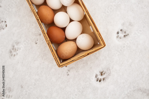 Chicken eggs folded into a wicker basket amid snow around traces of animals