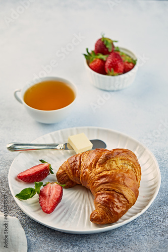 Croissant on a plate with strawberries and butter and a cup of tea