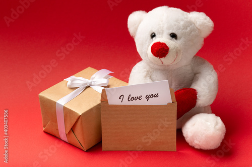 White teddy bear with hearts and gift box on red background, Valentine's day close up © Тетяна Шустик