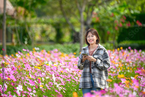 young woman Hold smart phone in flowering summer garden.woman in the garden of cosmos flowers field.