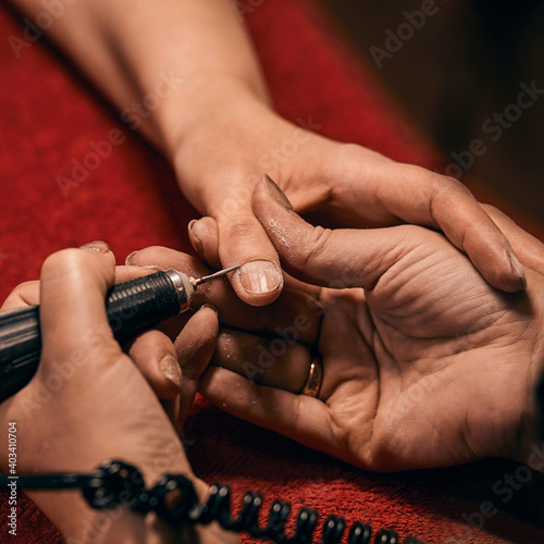 The girl does a manicure at home under the light of a lamp. Close-up of girl's hands with tool