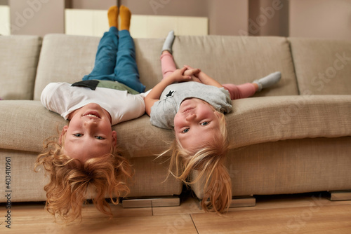 Have fun. Portrait of playful kids, little boy and girl lying upside down on a sofa in the living room