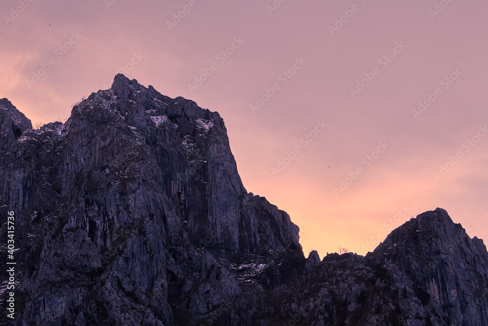 Pink and orange sunset behind a peak in a rocky mountain. 