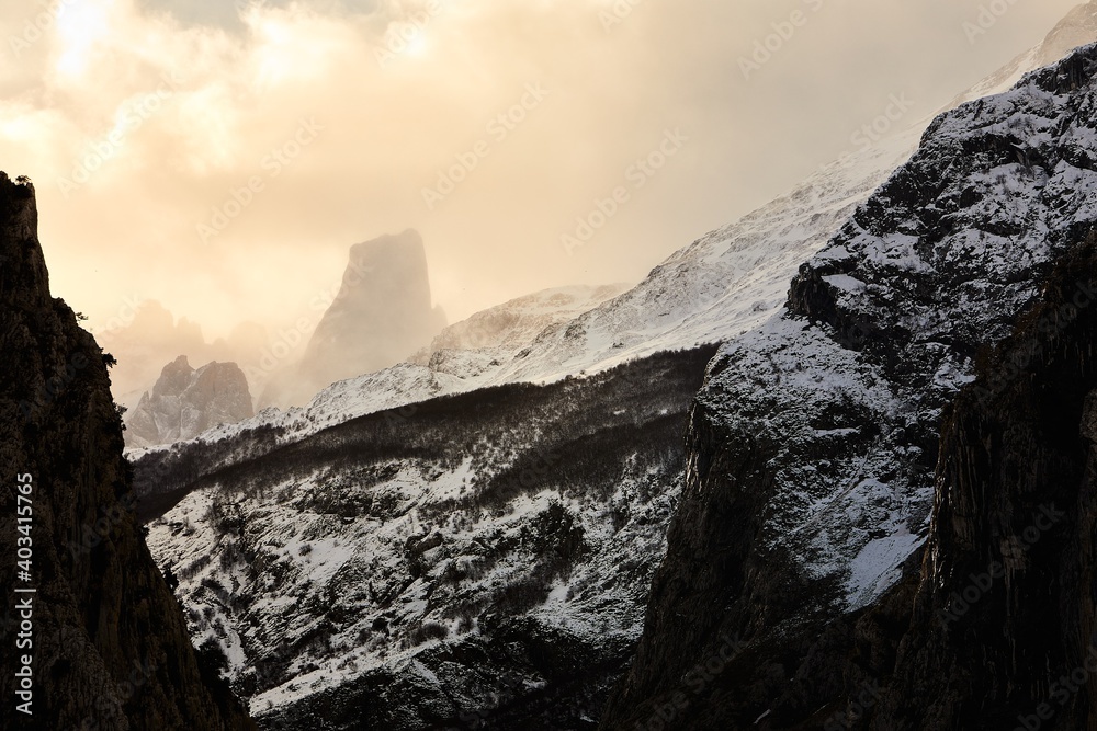 Beautiful snowy landscape in the middle of a mountain in a cloudy and sunny day. You can see a couple of birds flying. 