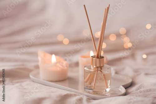 Home aroma fragrance diffuser with burning candles on white tray in bed over glowing lights close up. Cozy atmosphere. Wellness. Healthy lifestyle. photo