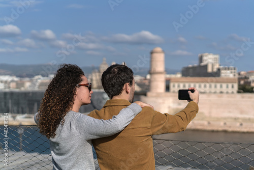 Jeune couple prend une photo au smartphone du vieux port de Marseille depuis les jardins du Pharo. On voit le MUCEM dans le fond