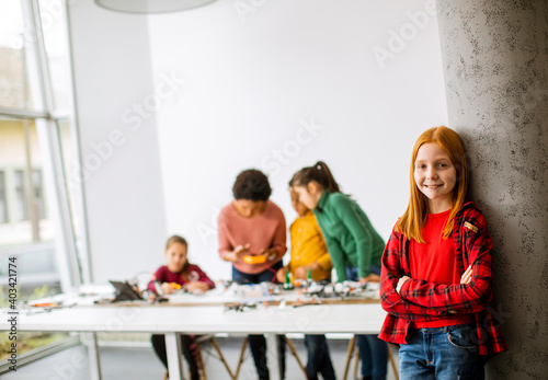 Cute little girl standing in front of kids programming electric toys and robots at robotics classroom
