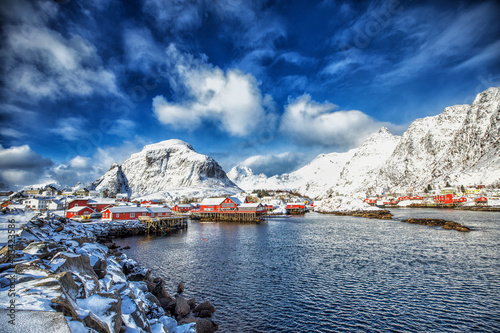 Norway. Lofoten. The village is on the water in the background of mountains and blue sky.