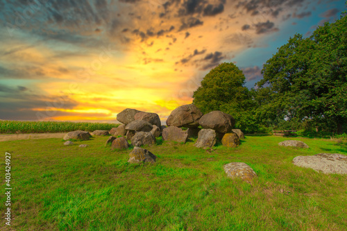 Dolmen D 15 in the province of Drenthe in the Netherlands with a background of oak trees and a beautiful Dutch cloudy sky during suwith blue spots. A dolmen is construction work from the new stone age