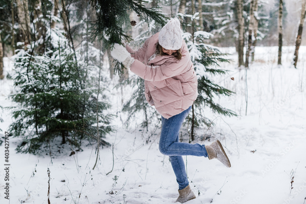 in a snowy forest, a beautiful girl pulls a branch of a snowy fir and snow falls on her