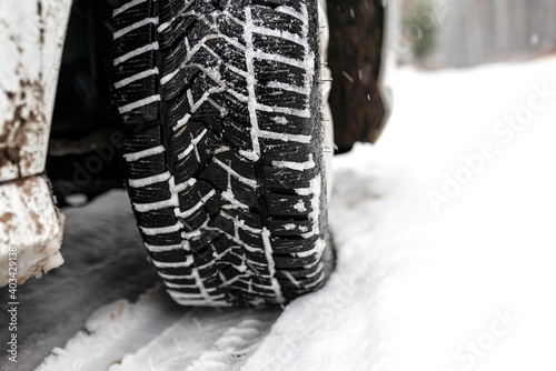 New winter tire in a silver car standing on a snow-covered road in the forest, a visible tread with snow. © Michal