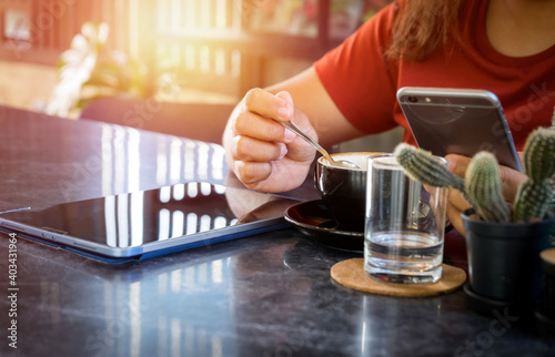 Young woman sitting in coffee shop at table,Female holding phone and looking on his screen in coffee shop. drinking coffee and using smartphone working with a tablet,The concept of the business idea.