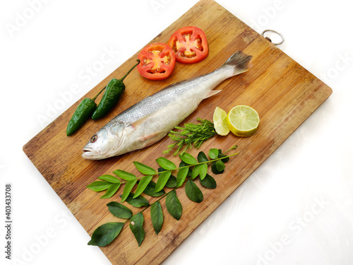 Fresh Silver Croaker Fish decorated with fruits and herbs on a wooden pad,Selective Focus.White Background. photo