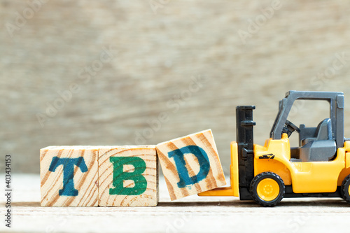 Toy forklift hold letter block d to complete word TBD (Abbreviation of to be defined, discussed, determined, decided, deleted or declared) on wood background