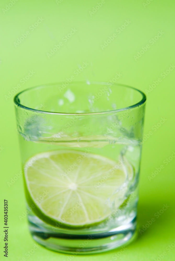 Limettenscheibe im Wasserglas vor gr¸nem Hintergrund Limettenscheibe im Wasserglas vor gr¸nem Hintergrund