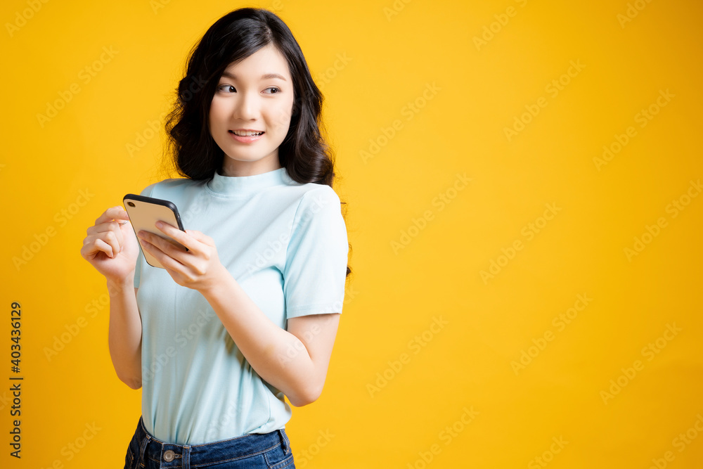 Young woman standing alone with mobile phone in hand portrait isolated on yellow studio background Young woman standing alone with mobile phone in hand portrait isolated on yellow studio background