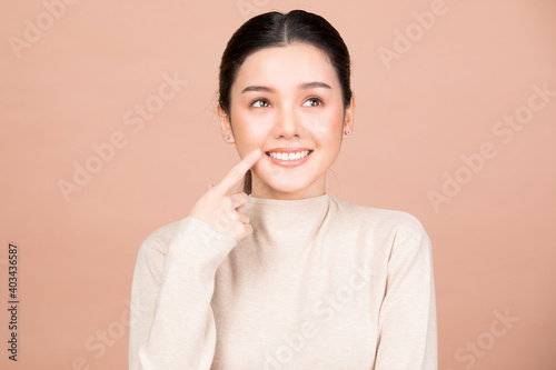 Portrait of smiling woman pointing at her nice teeth and mouth isolated on brown background
