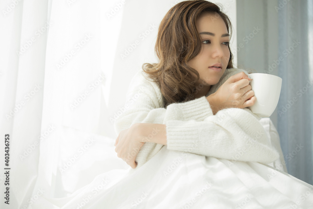 Sick woman sitting in bed with mug cup in hand